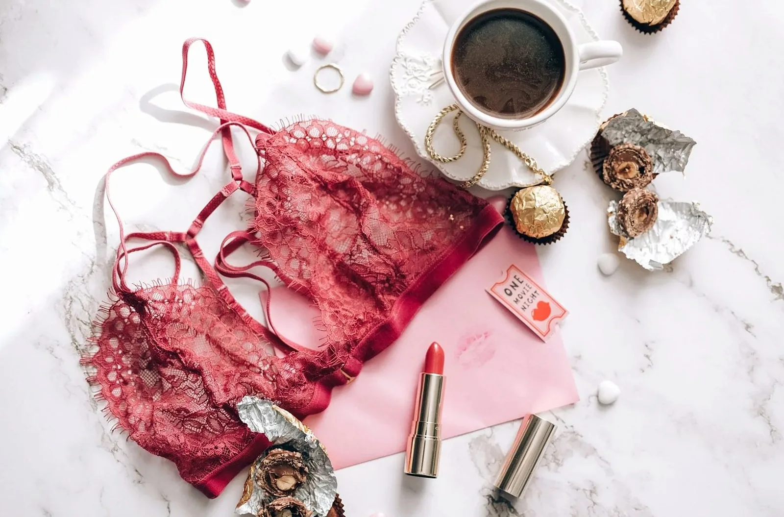 A chic flat lay featuring coffee, chocolates, and lace lingerie on a marble surface.