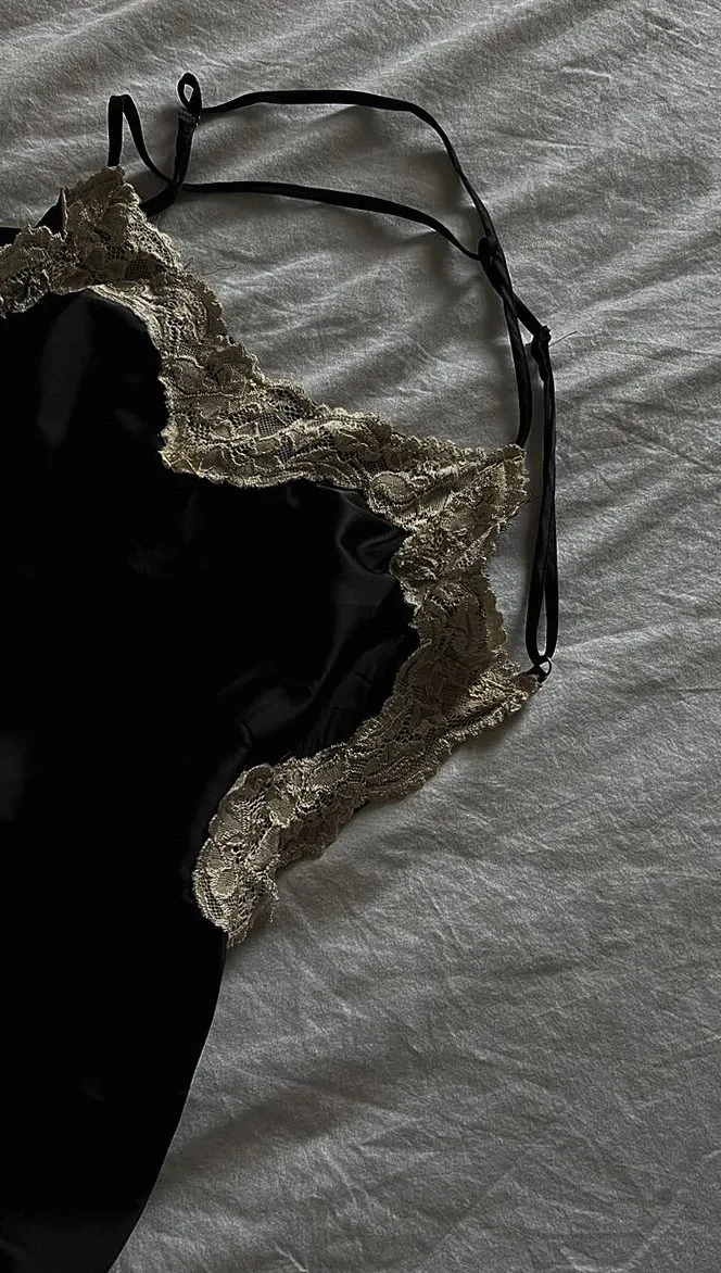 Close-up of a black satin dress with intricate lace detail on a bed.